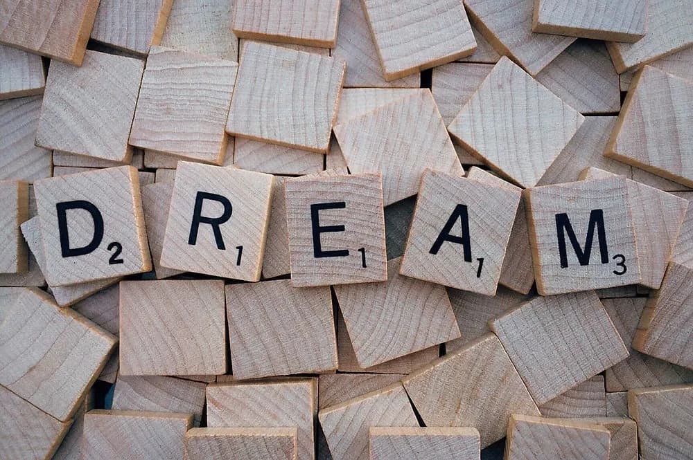 Деревянные плитки с буквами, выложенные в слово DREAM, среди россыпи фишек