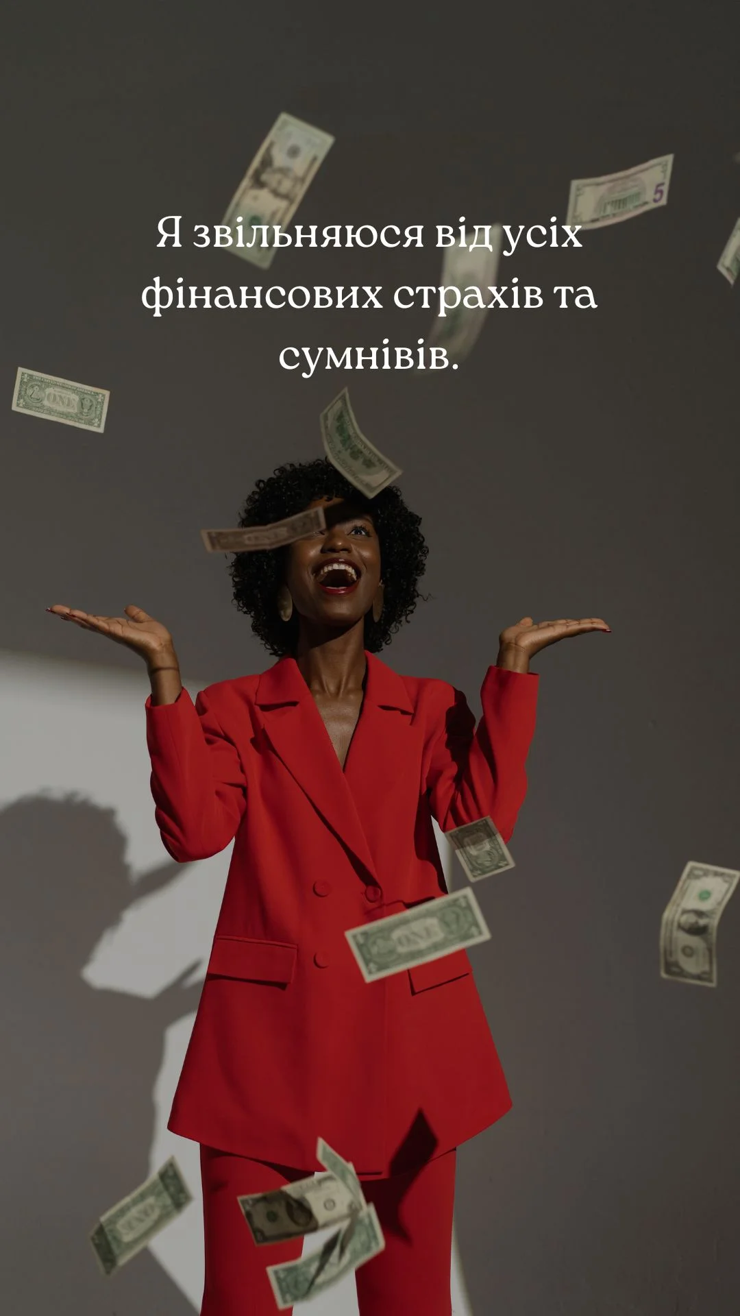 Картка грошової афірмації: жінка в червоному костюмі серед доларових купюр, що падають, із написом «Я звільняюся від усіх фінансових страхів та сумнівів.»