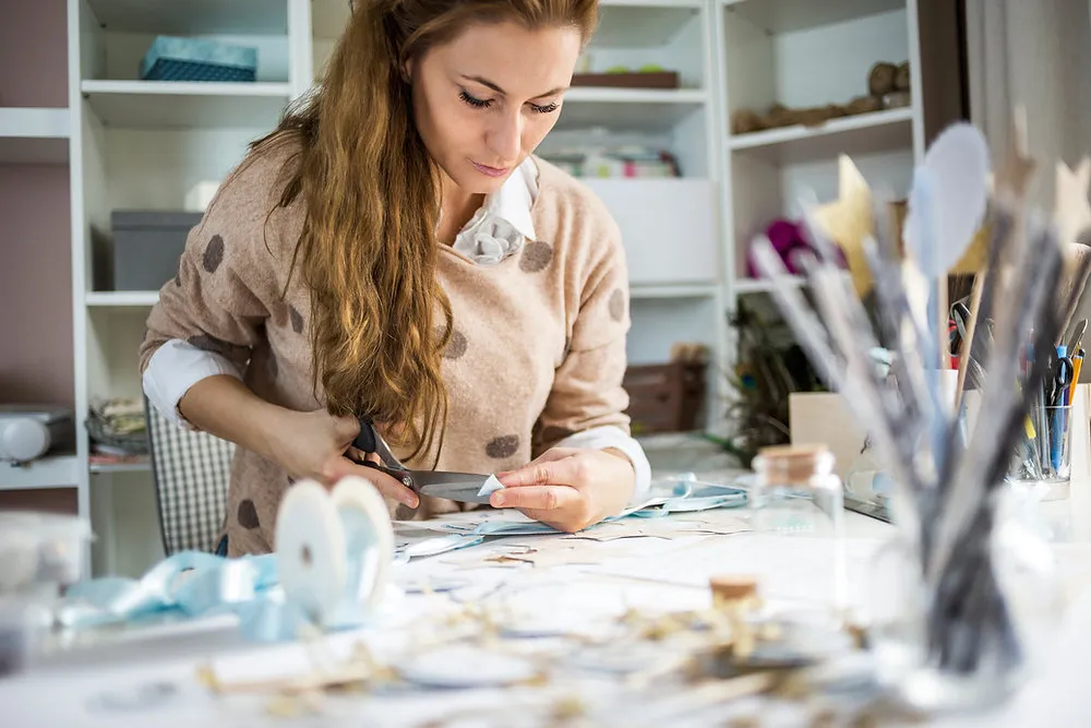 Woman at a craft table cutting out paper clippings with scissors to make a handmade vision board