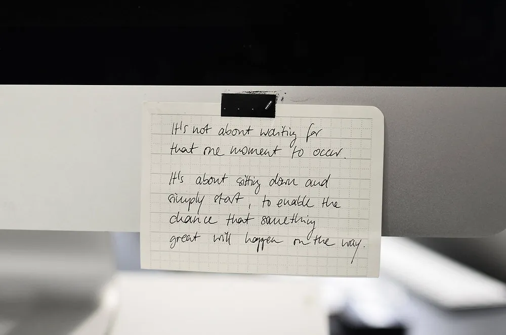 Handschriftliche Notiz auf kariertem Papier am Bildschirm: nicht auf den perfekten Moment warten, sondern einfach anfangen