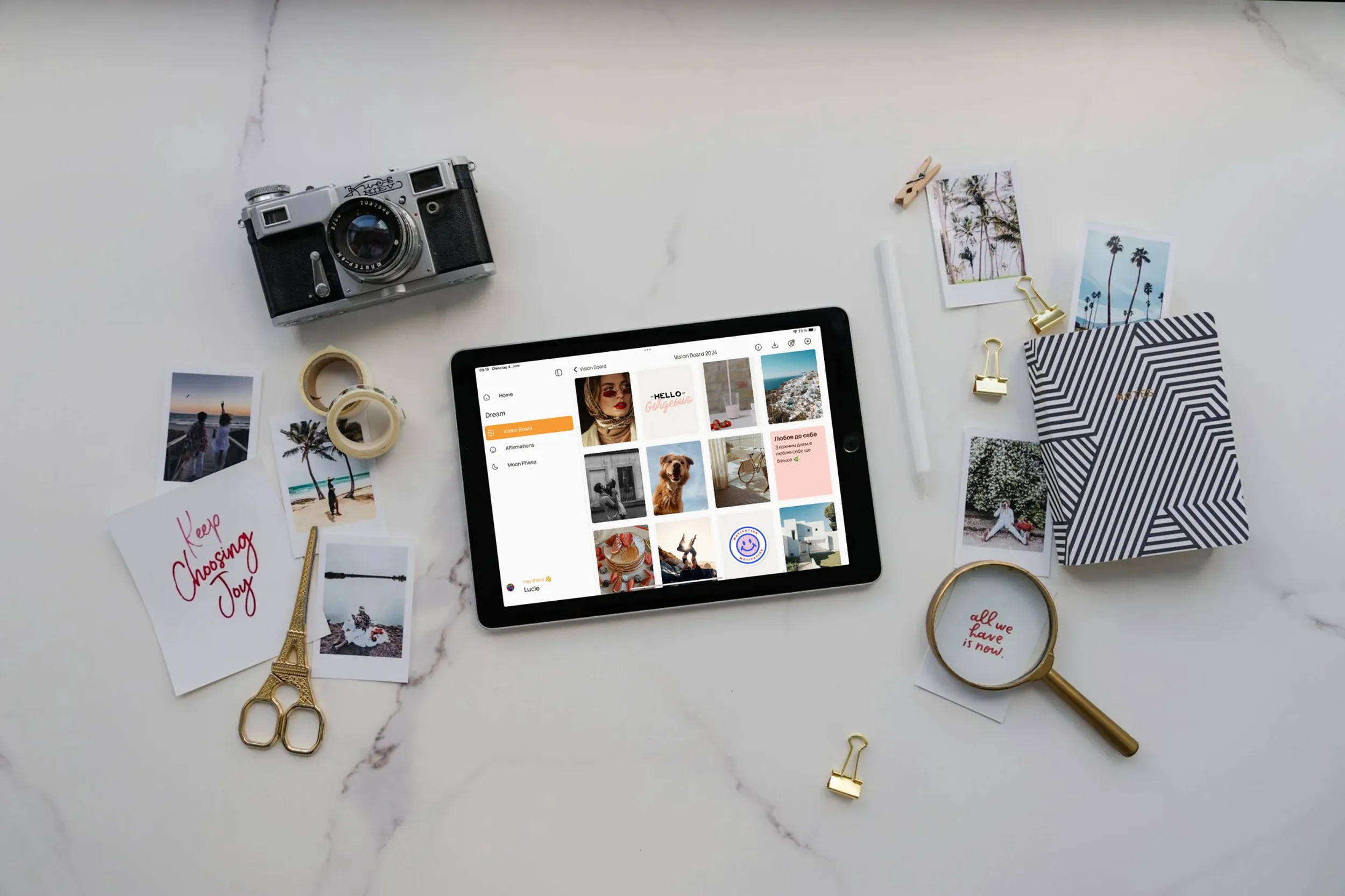 VISIYA vision board open on an iPad amid a vintage camera, gold scissors, washi tape and printed photos on white marble