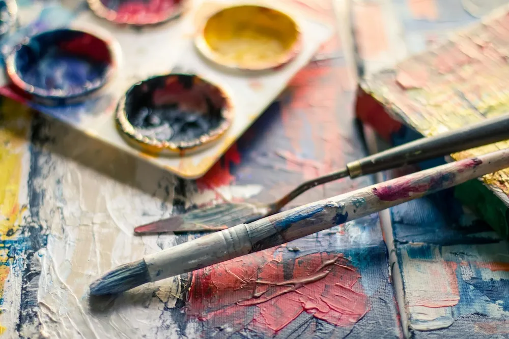 Aquarellfarben und gut genutzte Pinsel auf einer bunt bemalten Leinwand