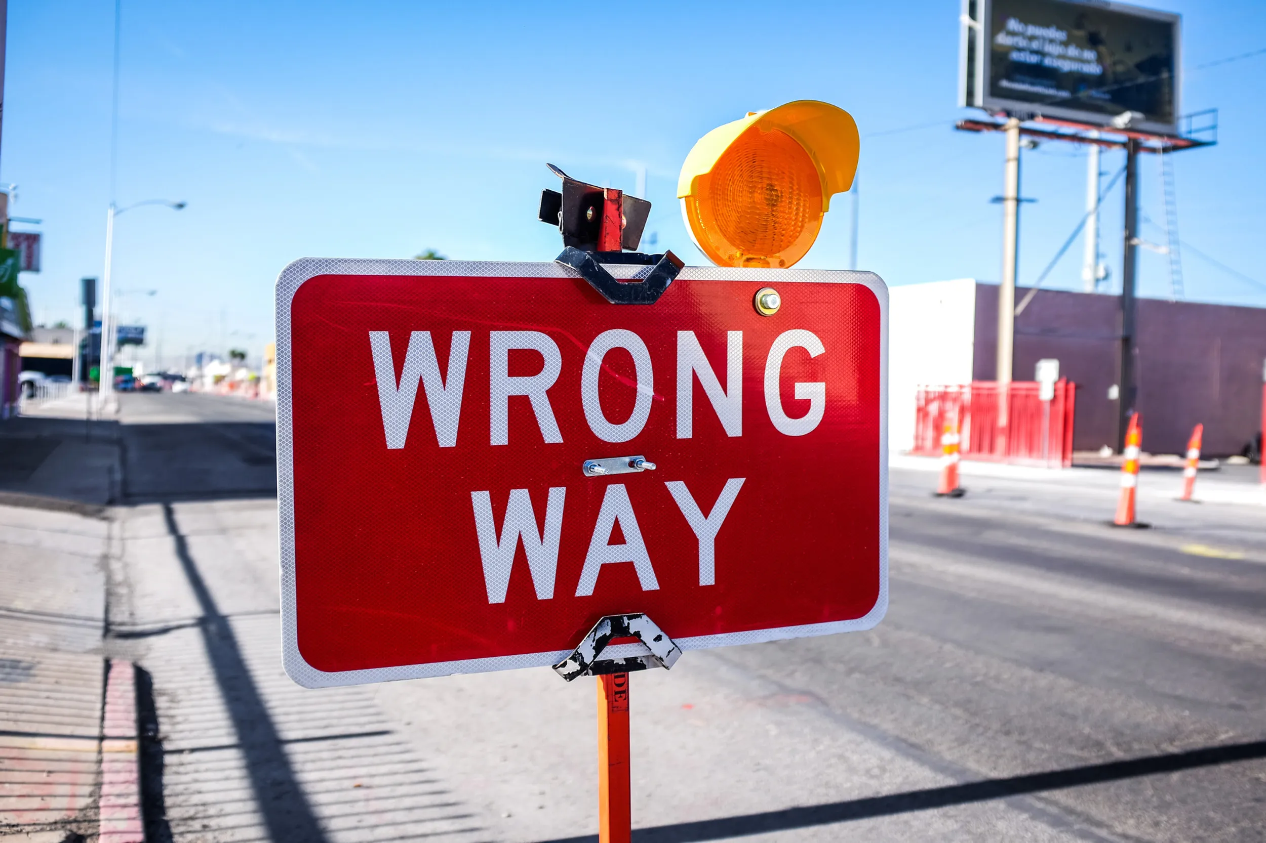 Rotes Straßenschild mit der Aufschrift 'WRONG WAY' vor blauem Himmel an einer Kreuzung