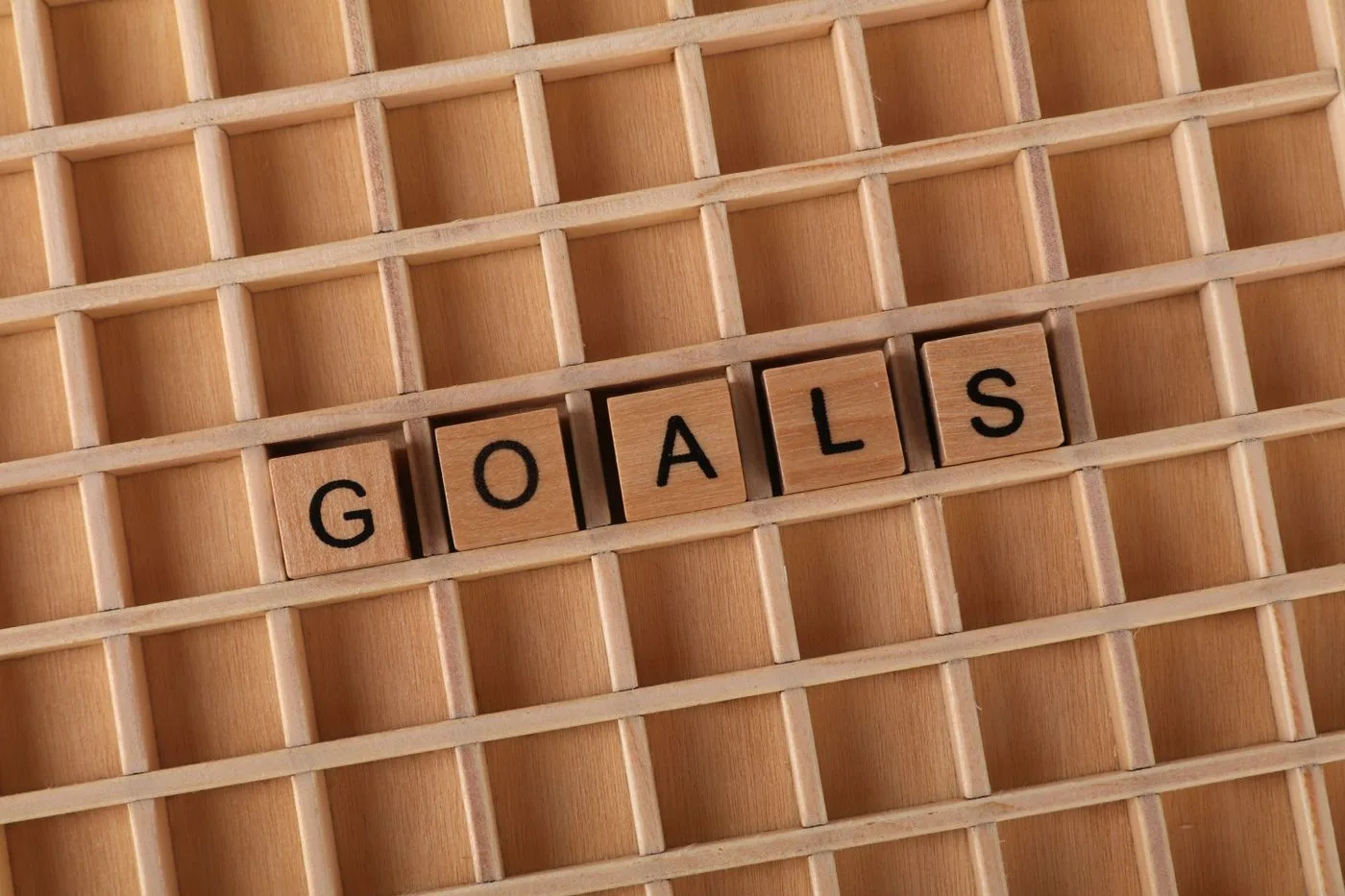 Дерев'яні кубики з літерами, що складають слово «Goals», на дерев'яній решітці