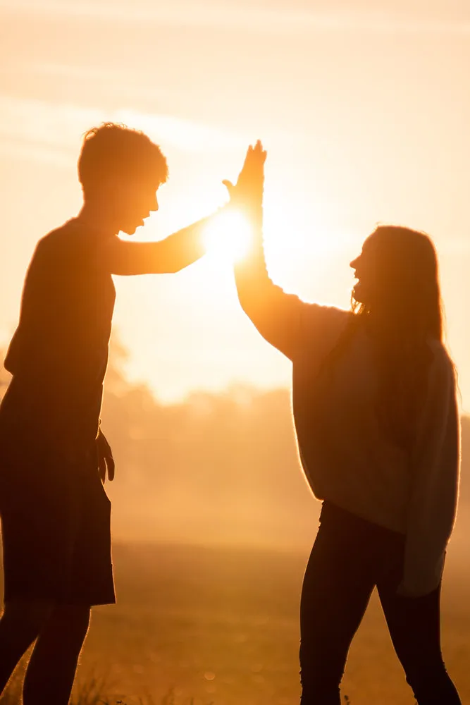 Two people silhouetted against a golden sunset giving each other a high five in an open field