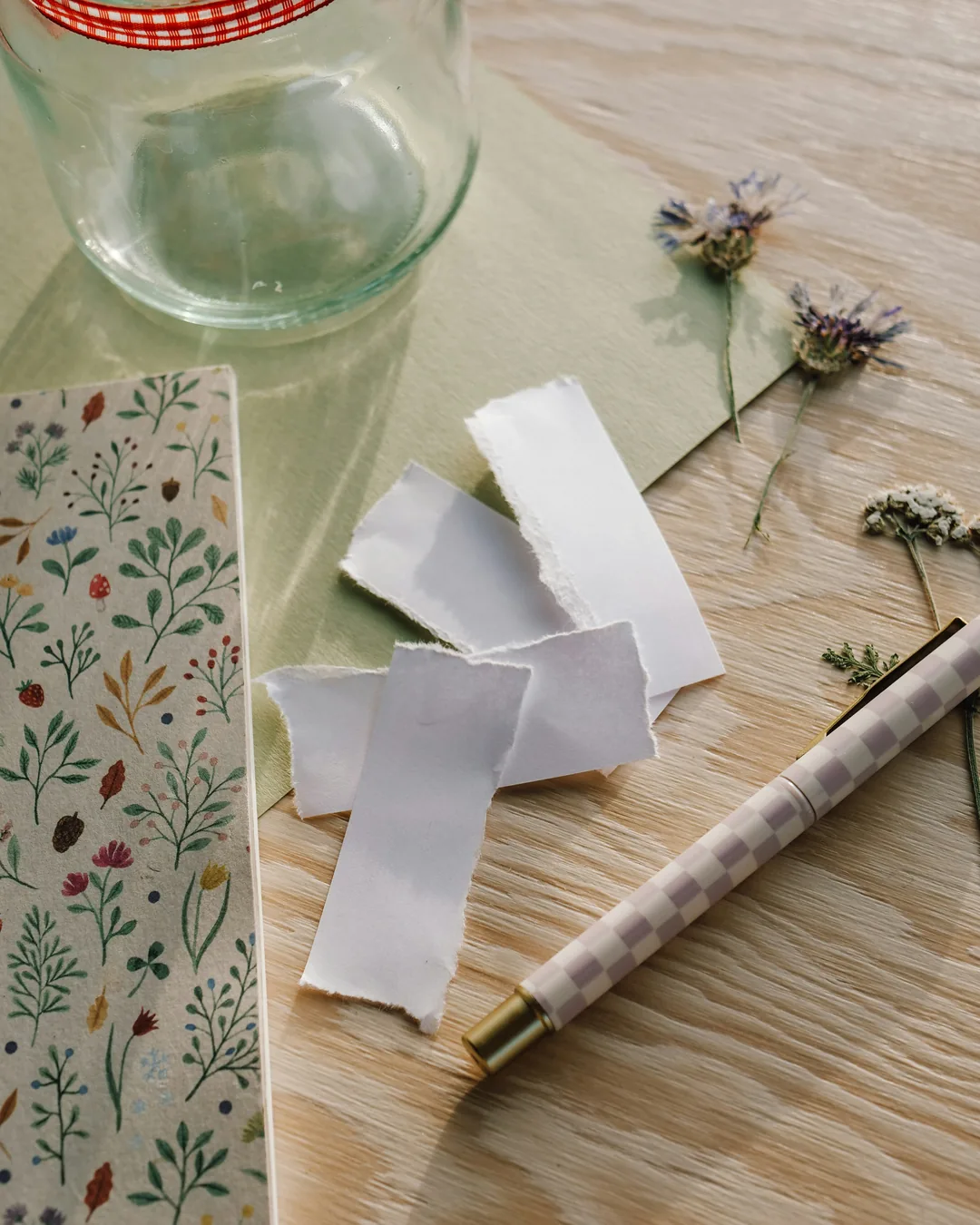 Blank paper slips, a pen and an empty glass jar on a light wooden table