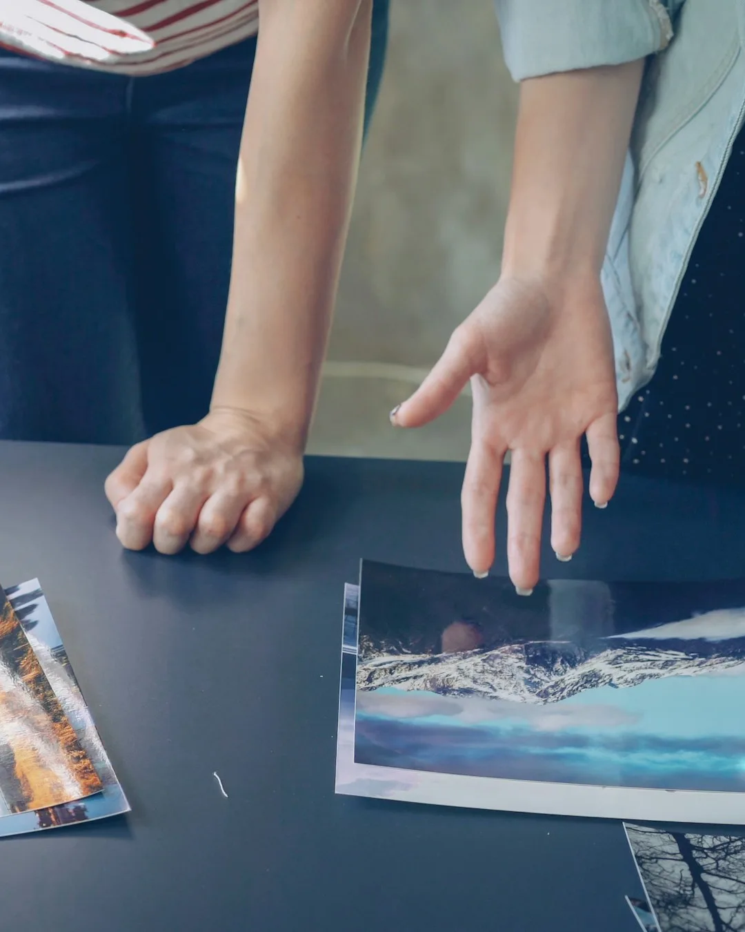 Hands spreading out printed photos on a dark table before anything is glued