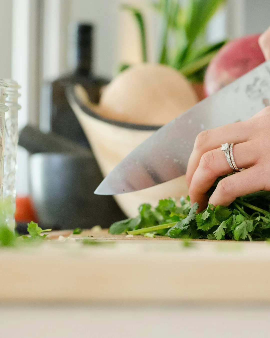 A woman's hands chopping fresh cilantro on a wooden board in a bright kitchen