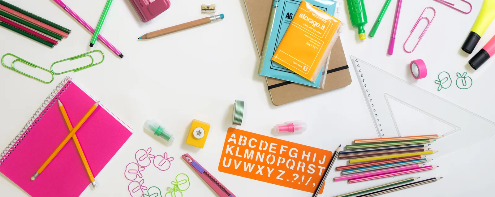 A colourful flat-lay of vision-board supplies: coloured pens, pencils, paper clips, scissors, notebooks and washi tape