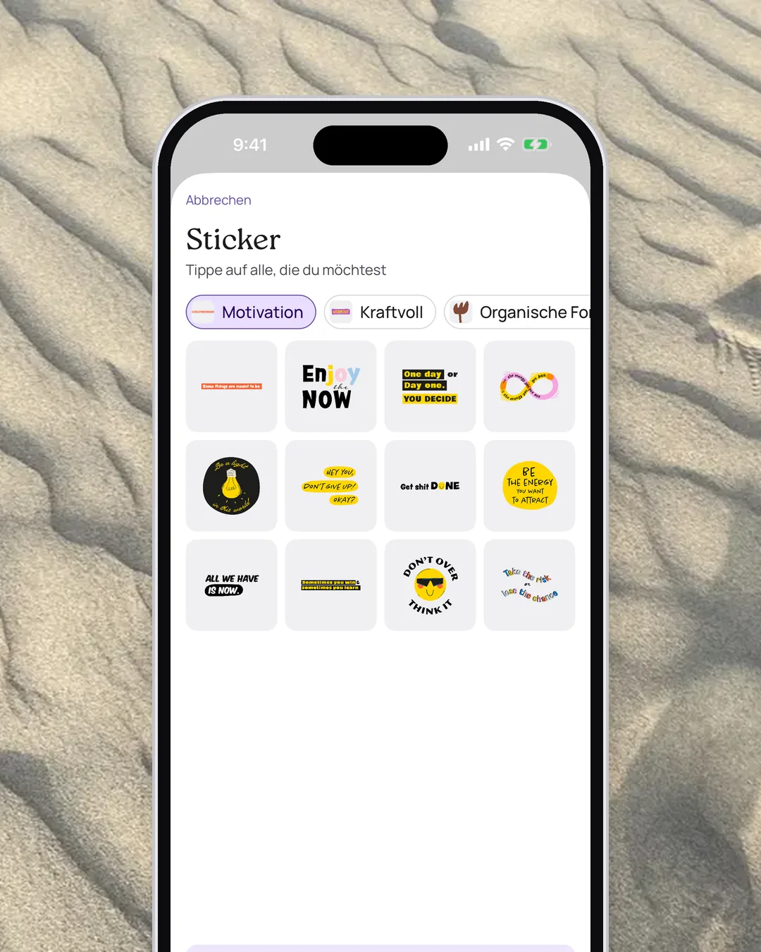 Sticker-Pakete in VISIYA mit kurzen Sprüchen, auf einem iPhone über gewelltem Sand