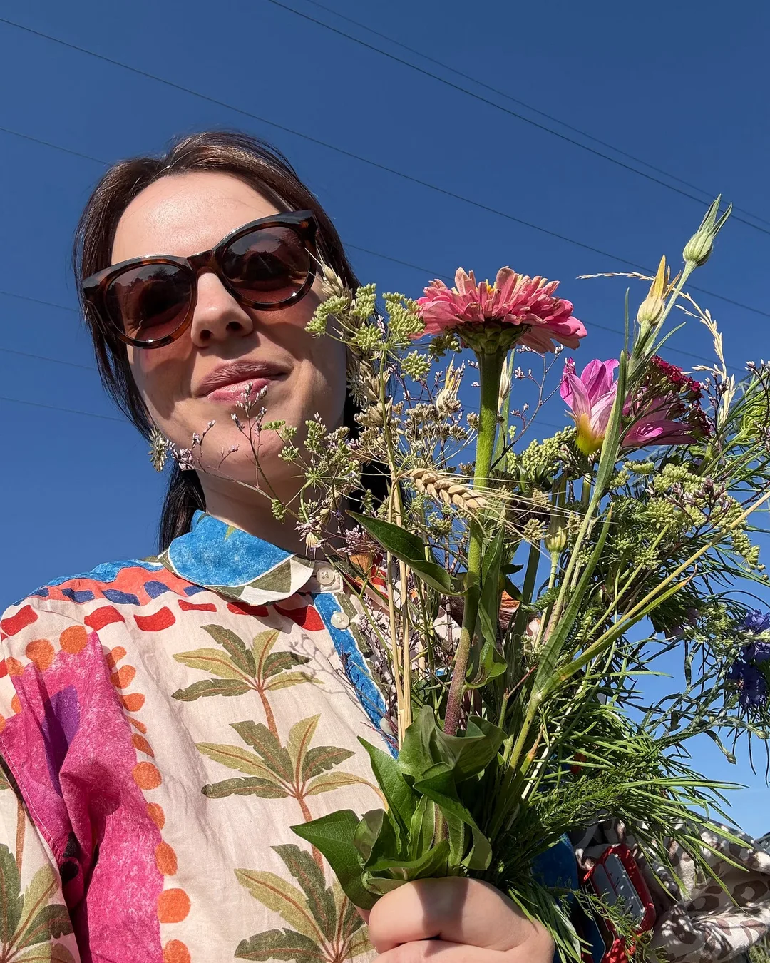 Me in sunglasses holding a bouquet of wildflowers against a blue sky: one of my six summer wishes