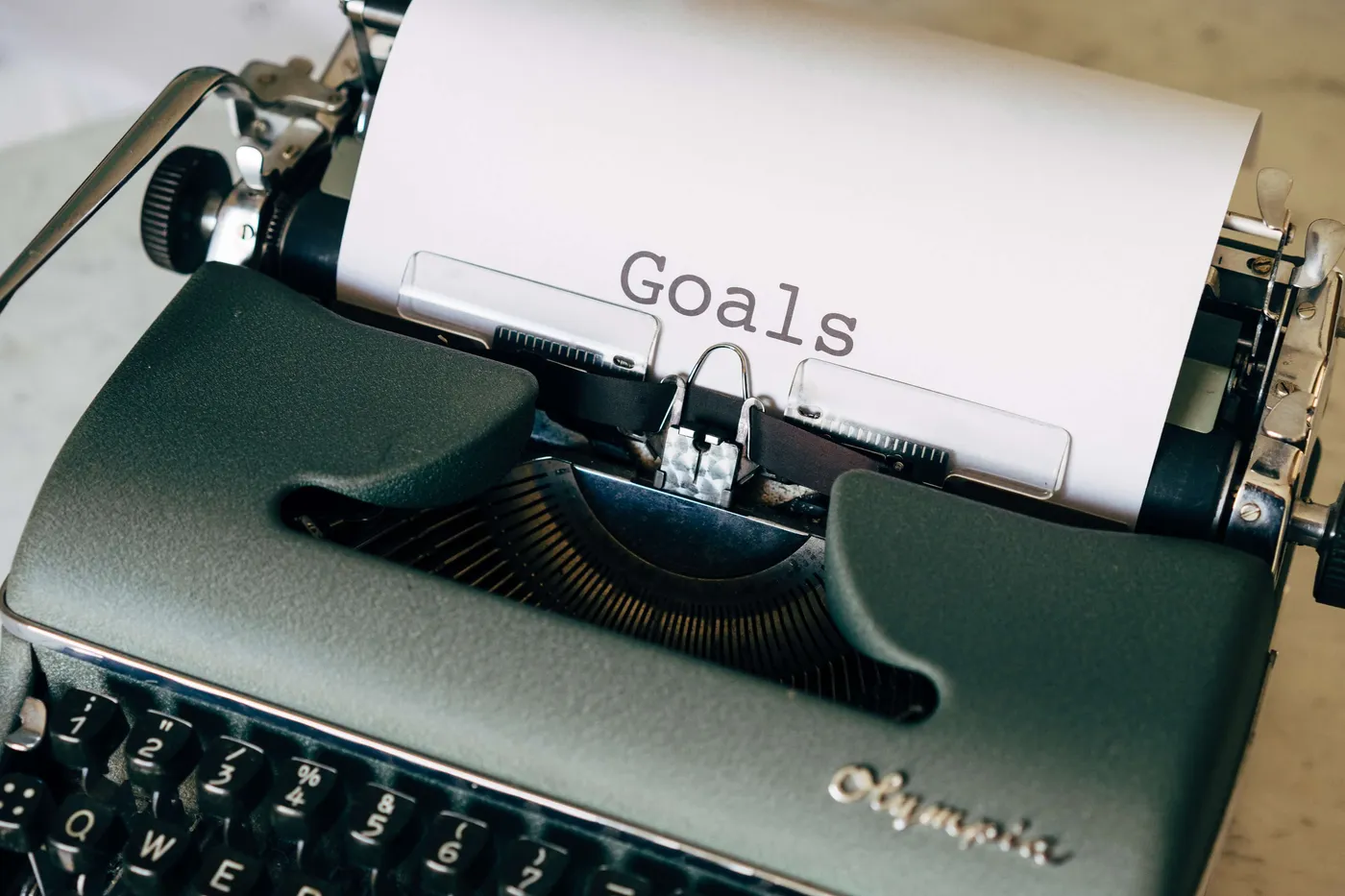 Eine grüne Vintage-Schreibmaschine der Marke Olympia mit einem Blatt Papier, auf dem nur das Wort 'Goals' steht