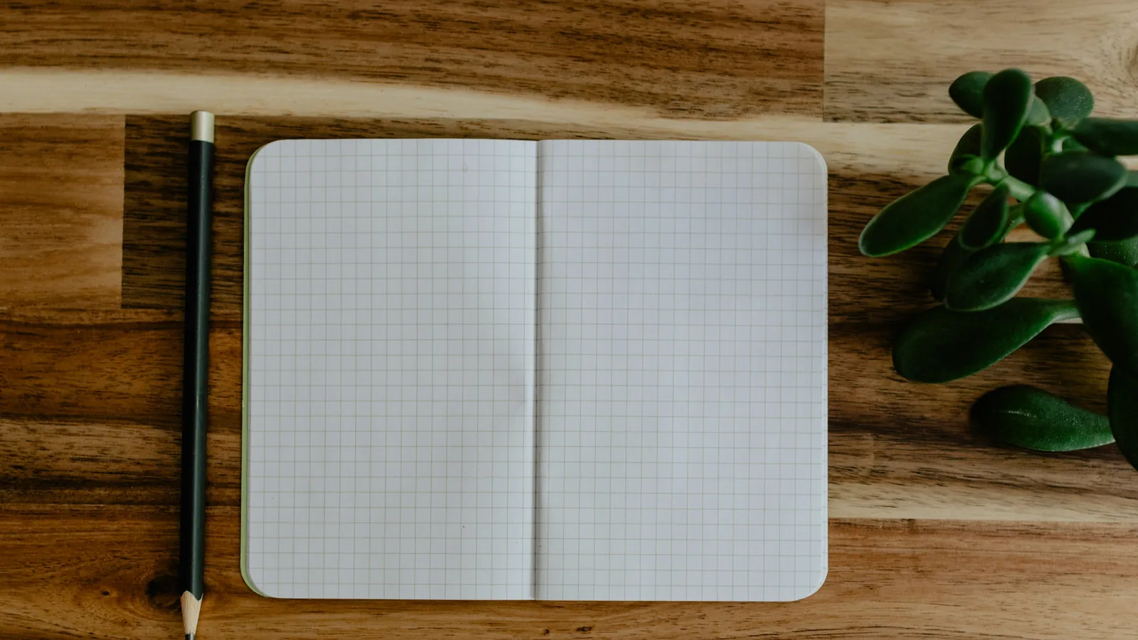 An open notebook with blank grid pages and a pencil on a wooden table