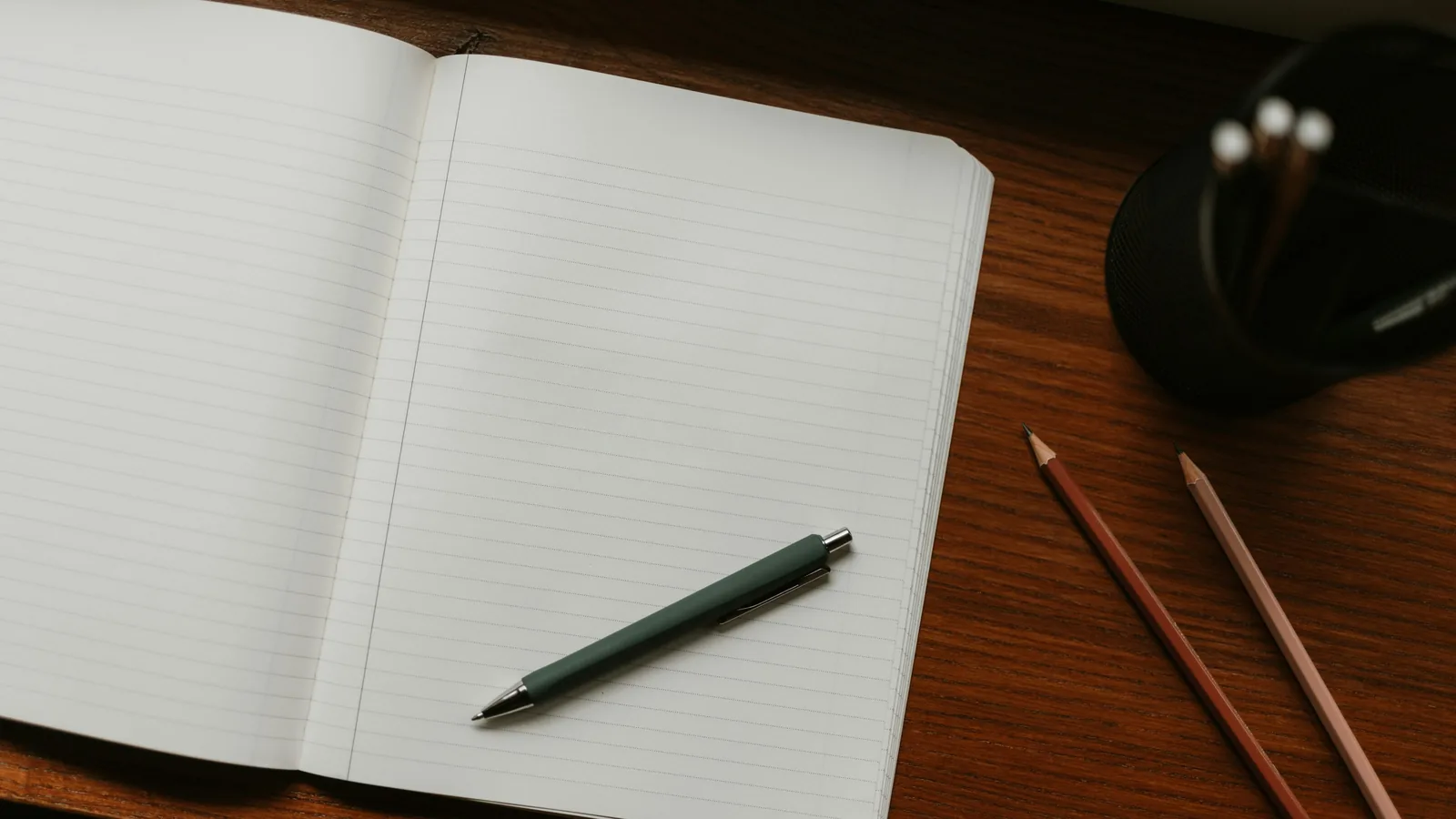 Ein aufgeschlagenes, leeres Notizbuch mit Stift und zwei Bleistiften auf einem Holzschreibtisch