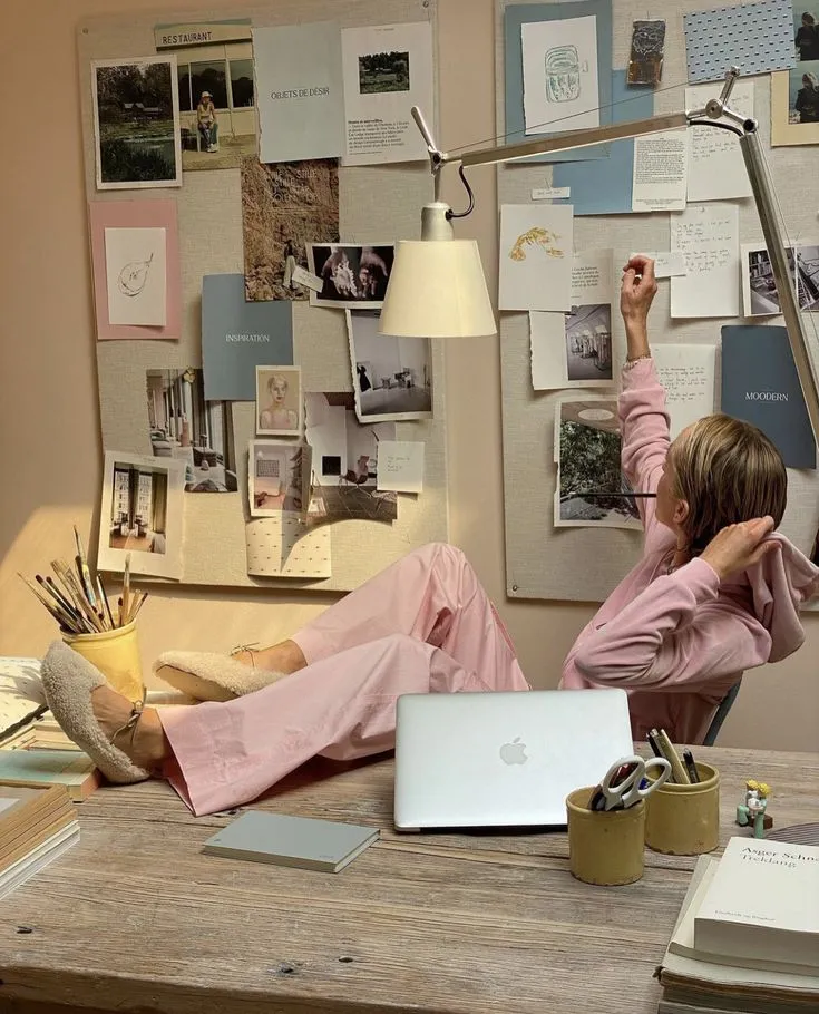 Eine Frau entspannt an ihrem Schreibtisch neben Vision Board und Laptop