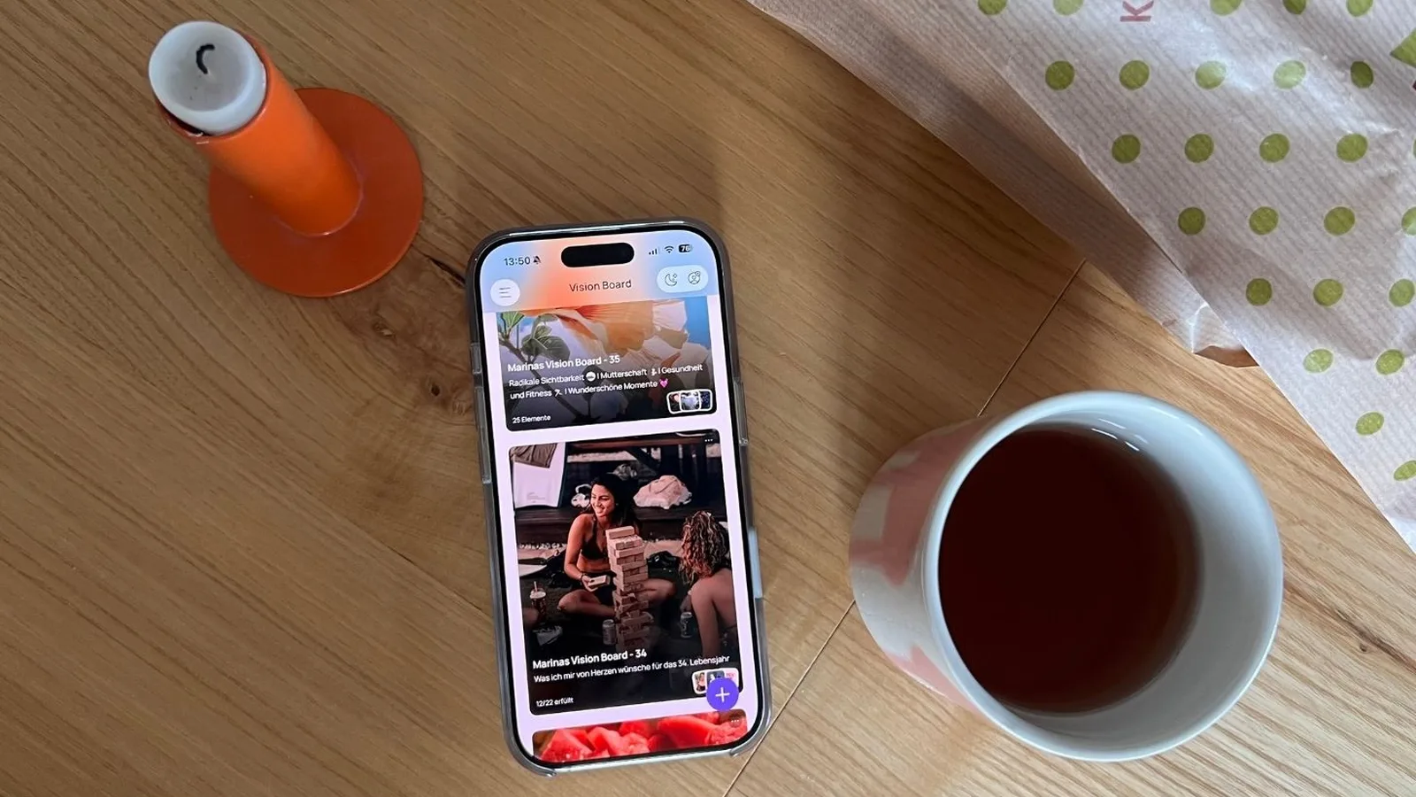 Marina's iPhone showing her two yearly boards in VISIYA, with the app in German: “Marinas Vision Board – 35” with her motto “Radikale Sichtbarkeit” (radical visibility) underneath, and “Marinas Vision Board – 34” marked “12/22 erfüllt” (12/22 fulfilled), next to a candle and a cup of tea