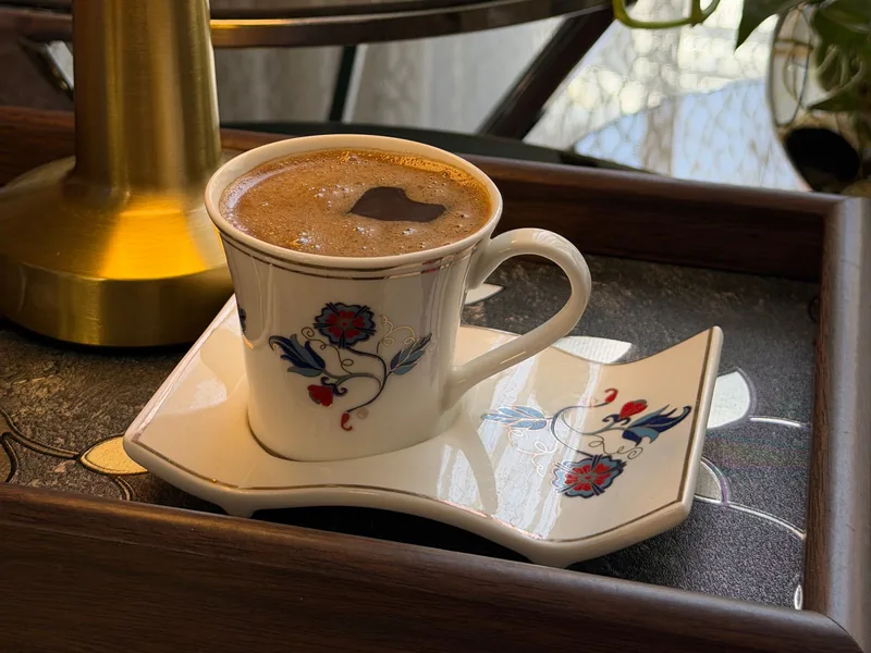 Eine Tasse Kaffee auf einem verzierten Tablett neben einer Messinglampe im weichen Abendlicht