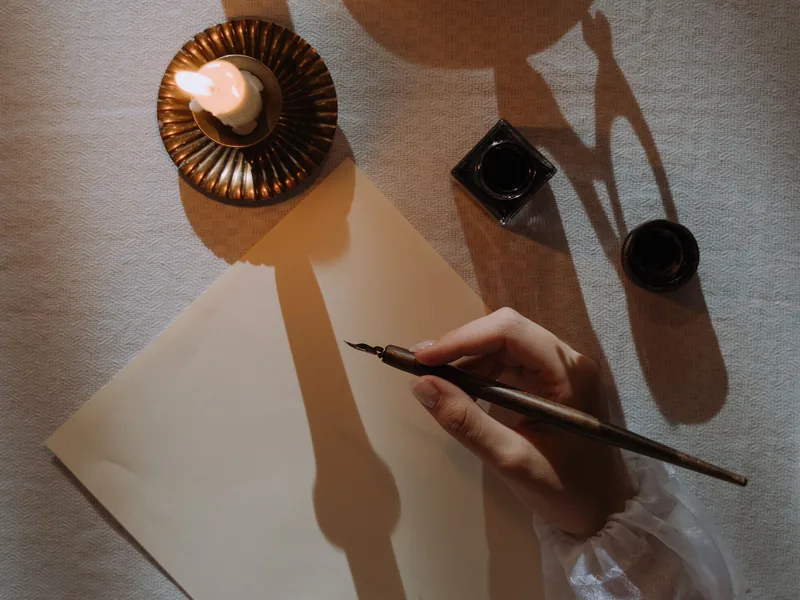 Eine Hand hält eine Schreibfeder über ein leeres Blatt Papier