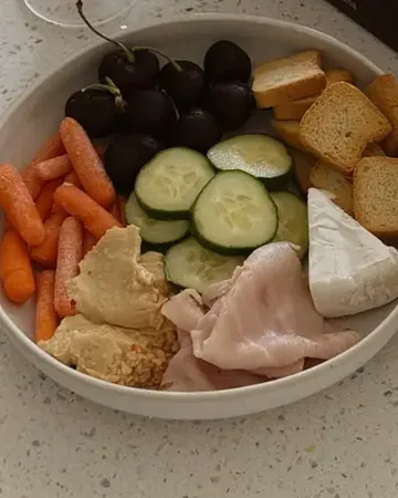 A bowl of carrots, cucumber, grapes, hummus, crackers and cheese