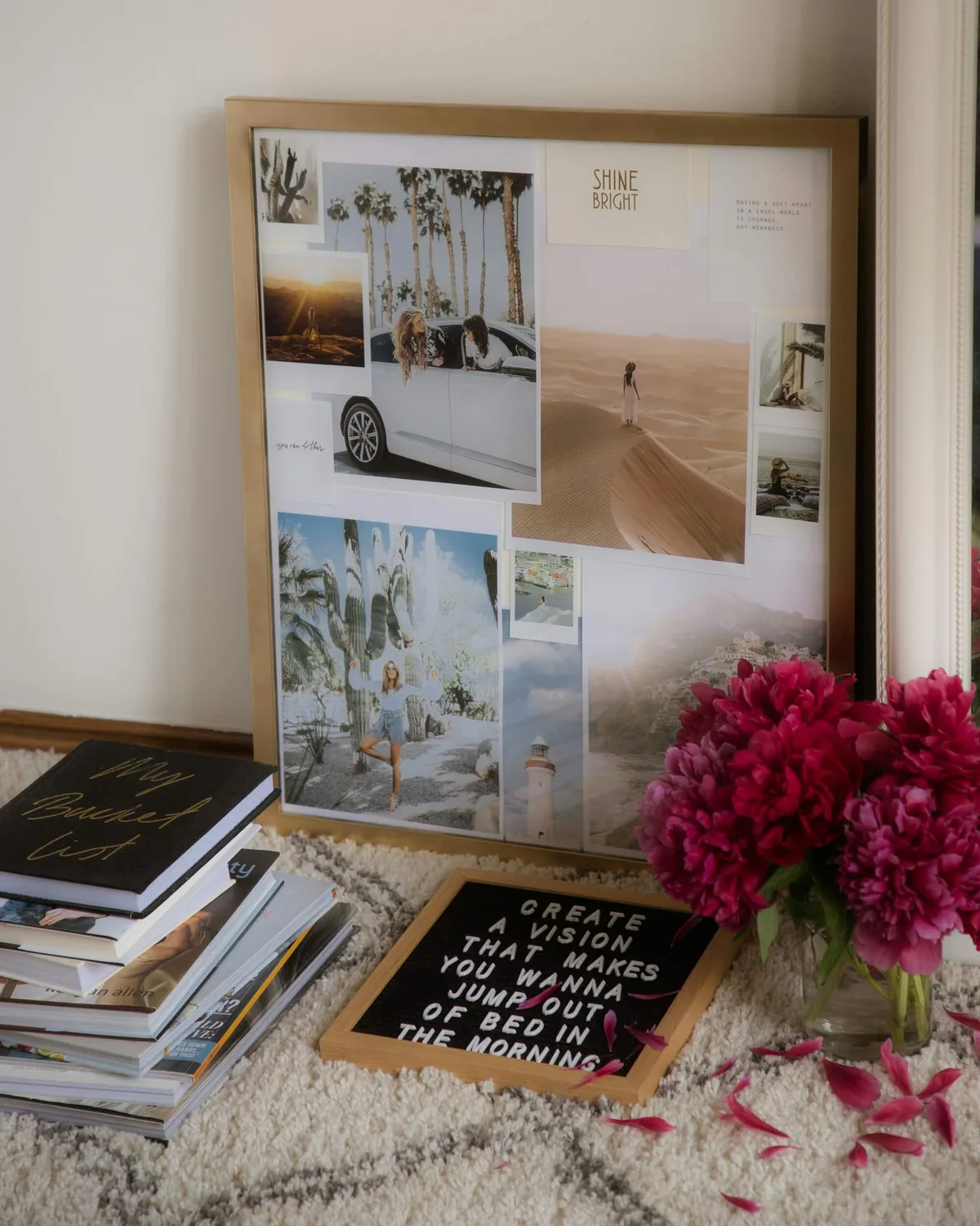 A vision board leaning against a wall, with books, peonies and a letter board in front of it